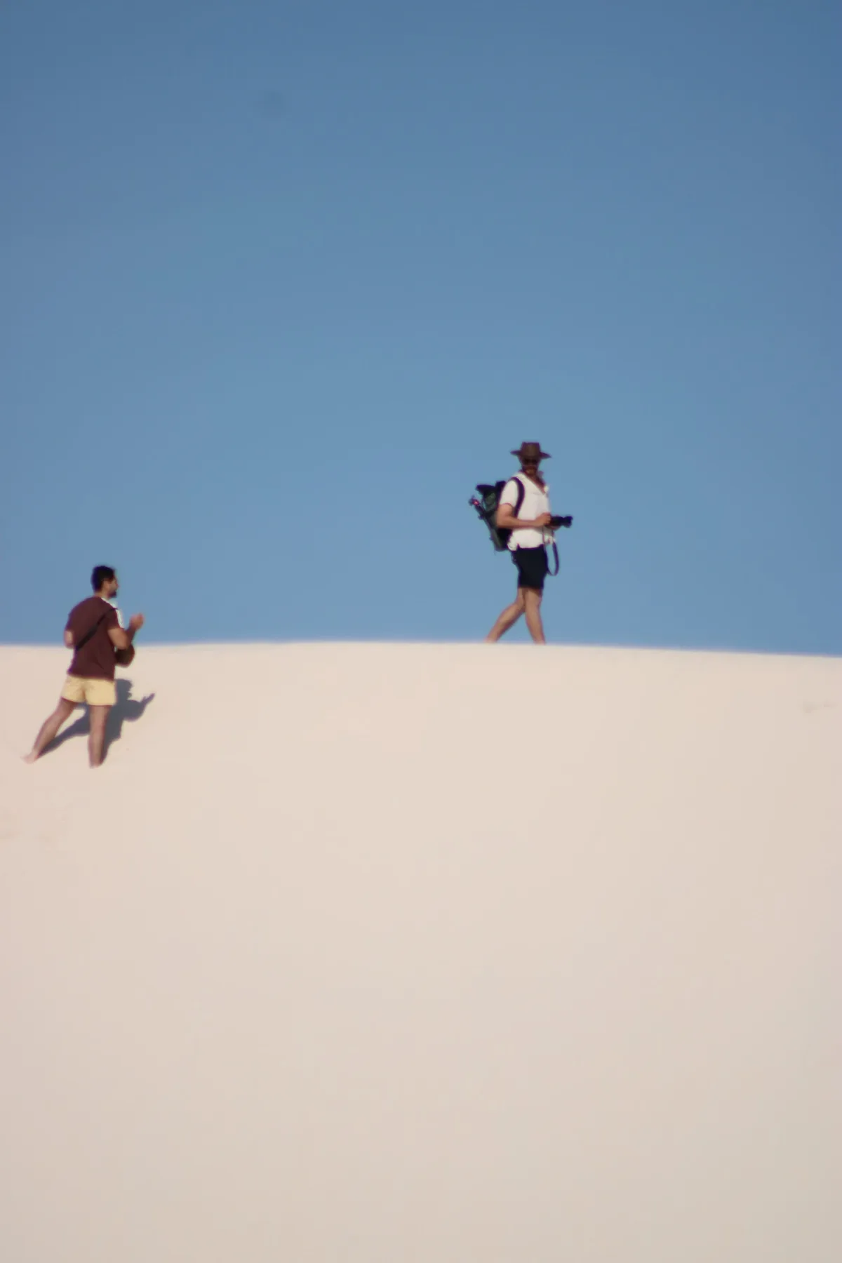 Visitantes caminham no alto das dunas dos Lençóis Maranhenses em dia de céu limpo e pouca gente