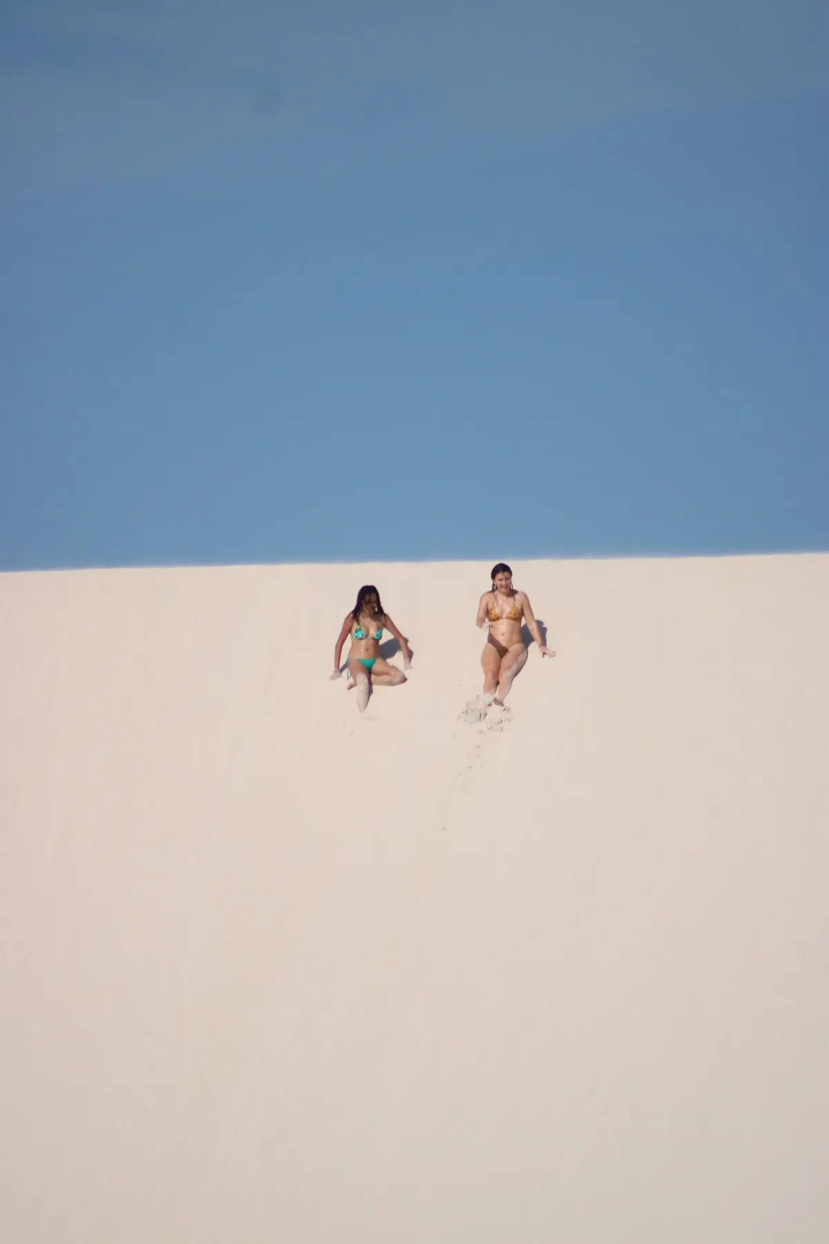 Duas visitantes descem uma duna branca quase vazia nos Lençóis Maranhenses fora da alta temporada